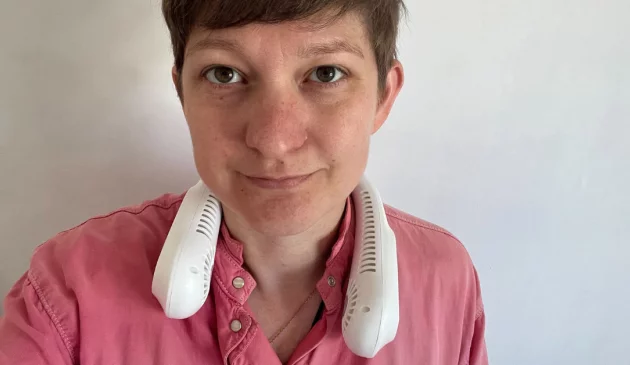 The author of this article, Poppy O'Neill, wearing a pink shirt and a white neck fan