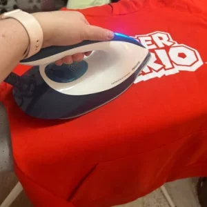 a hand ironing a red t shirt with a Philips PerfectCare Compact Steam Generator Iron