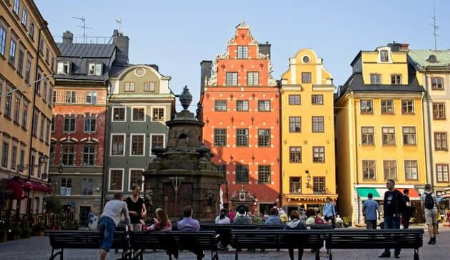 Colourful buildings in the city with benches and onlookers with a statue in the middle