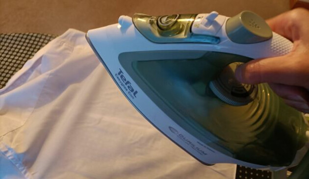 A hand coming from the right of the image holds the Tefal Easygliss Eco. A white child's shirt is laid out on the black and grey spotted ironing board.