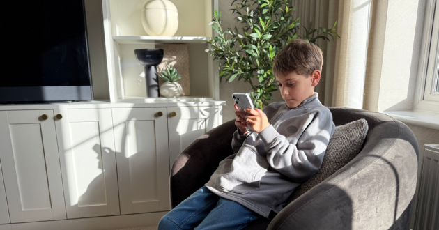 Child sitting in a living room using the Other Phone, illustrating everyday screen time and messaging on a child’s first smartphone with built-in SafetyMode protections