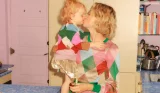 A mother and young daughter kissing while wearing festive jumpers from Boden