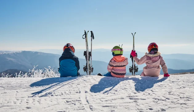 Heidi ski article main image showing three children in ski gear sitting on top of a mountain