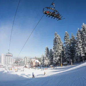Borovets, Bulgaria, snow-topped trees, ski piste, chair lift and resort under a blue sky
