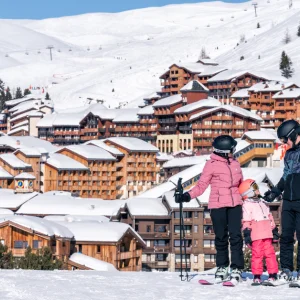 La Plagne, France - shot of family on slopes with resort buildings and ski lift in background. Photo credit: Brendan Le Peru