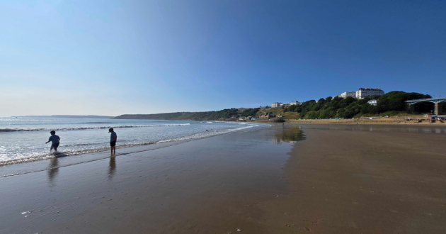 Children walk on the beach with the Esplanade Hotel Scarborough behind them on the cliff