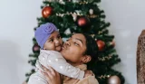 mother holds up baby in front of Christmas tree