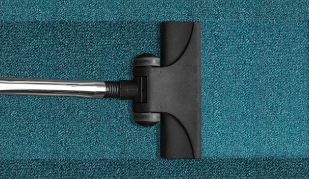 A black vacuum cleaner head on a teal carpet