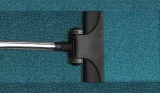 A black vacuum cleaner head on a teal carpet