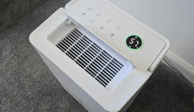 op of a white dehumidifier with the air outlet flap open, showing a round display reading 57 with a green ring above the touch controls, on grey carpet