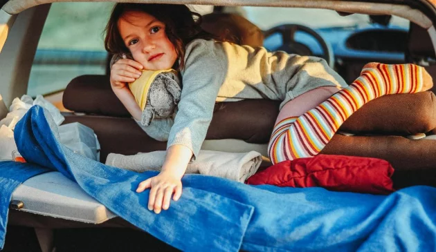 A girl in a car boot surrounded by luggage.
