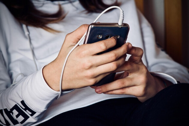 A close up on a teenage girl's hands holding a smartphone with headphones plugged in