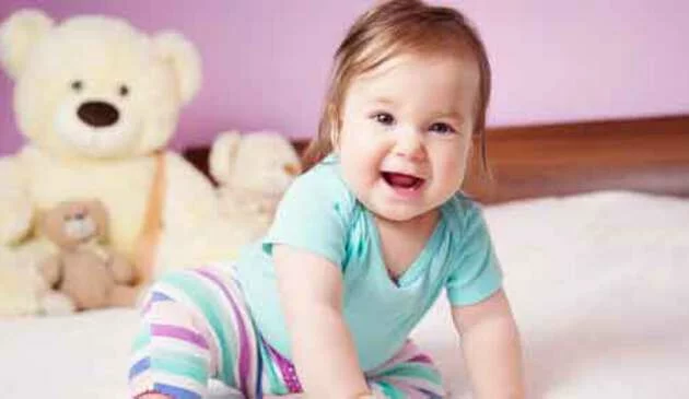 Baby sitting up and laughing on bed