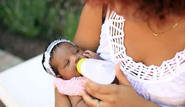 Small baby being held by mother and fed by bottle