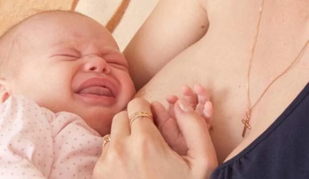 Baby crying with head on woman's breast