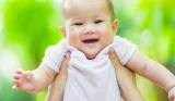 Baby being held in the air smiling at the camera