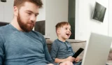 Dad on laptop while child enjoys TV