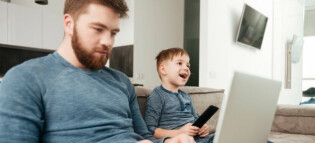 Dad on laptop while child enjoys TV