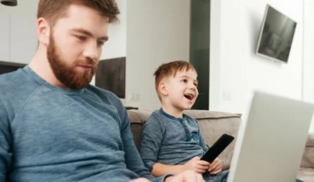 Dad on laptop while child enjoys TV