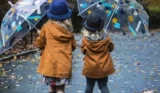 Two kids in raincoats, playing with umbrellas