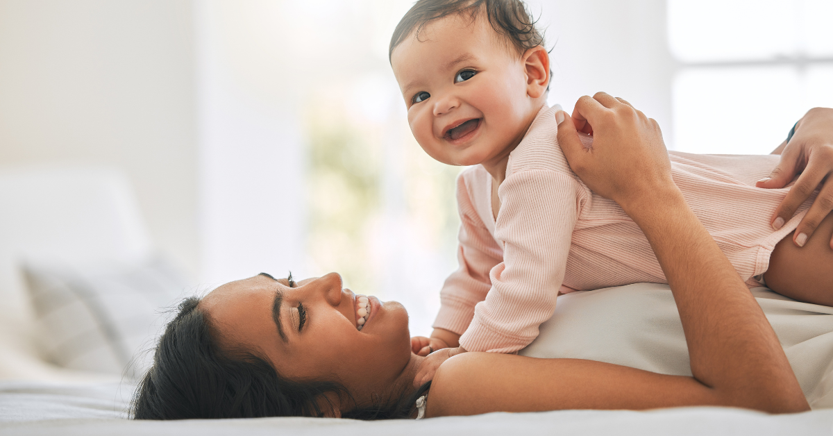 Mother cuddling smiling baby while laying down