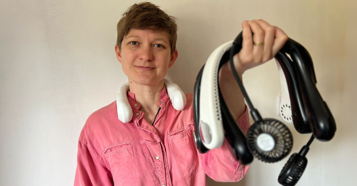 A woman with short hair and a pink shirt wearing a neck fan and holding several more neck fans in her hand