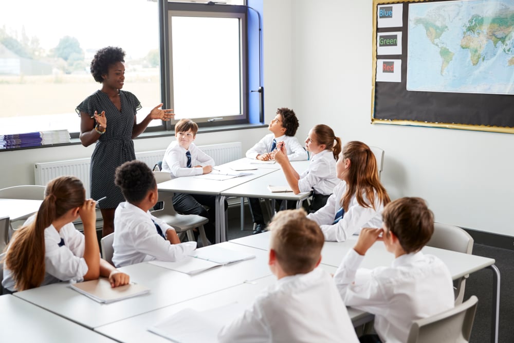 A teacher is stood up speaking to a room of students at school